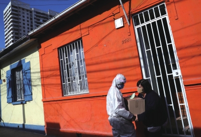 5月22日，在智利圣地亚哥，工作人员向一名女子发放食物和清洁用品。□新华社照片